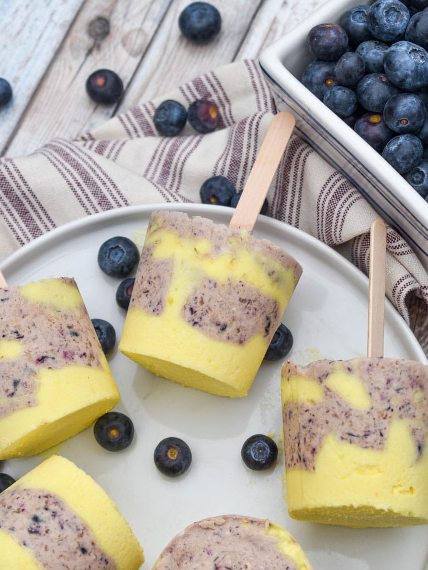 lemon blueberry pudding pops on a white plate with fresh blueberries on the side