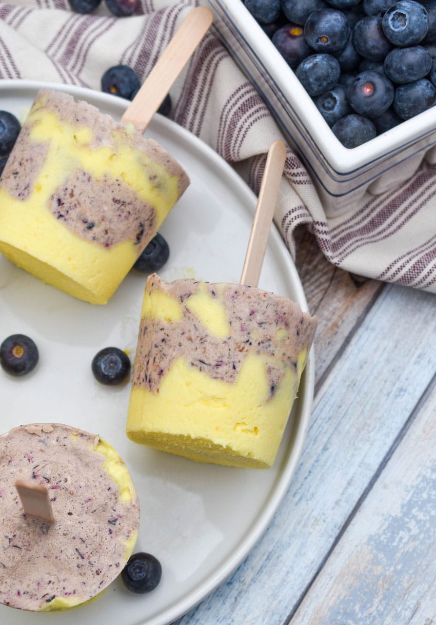 lemon blueberry pudding pops on a white plate with fresh blueberries on the side