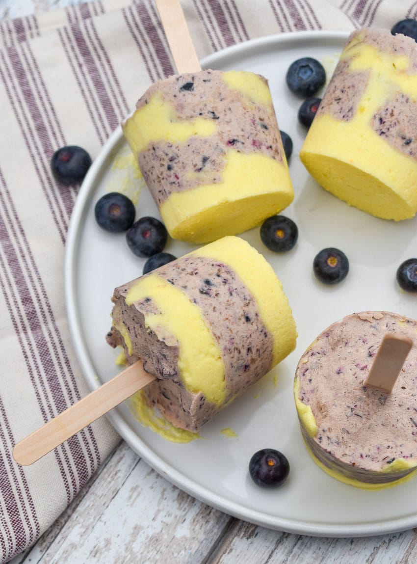 lemon blueberry pudding pops on a white plate with fresh blueberries on the side