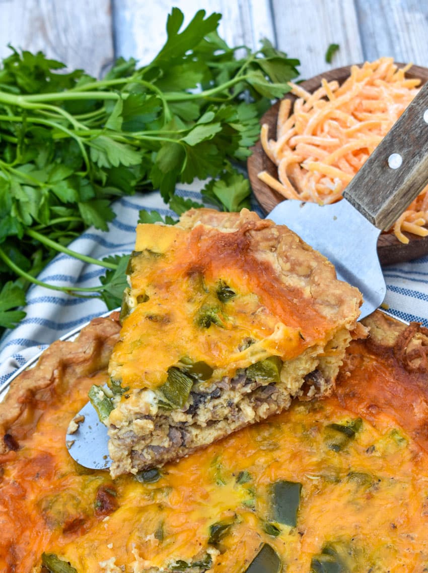 a wooden spatula lifting up a slice of a philly cheesesteak quiche