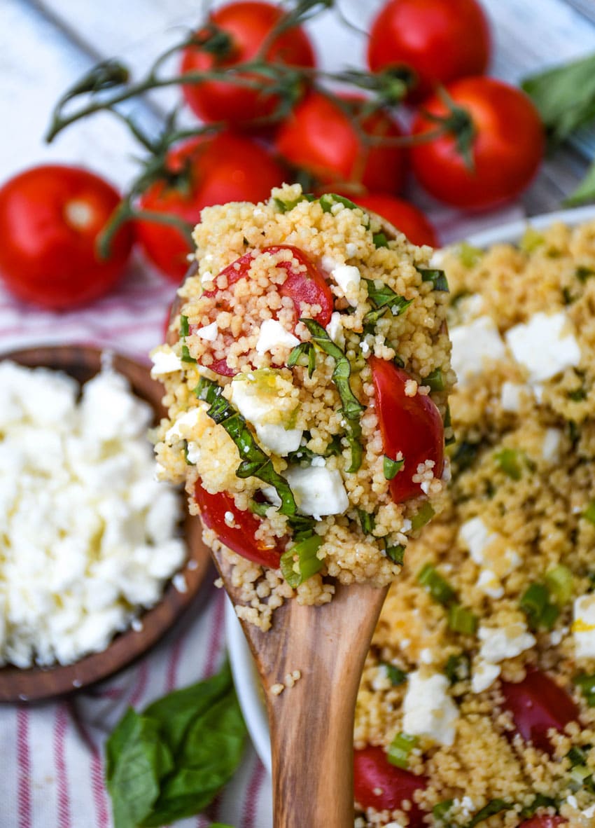 a wooden spoon holding up a scoop of fresh everything summer couscous salad