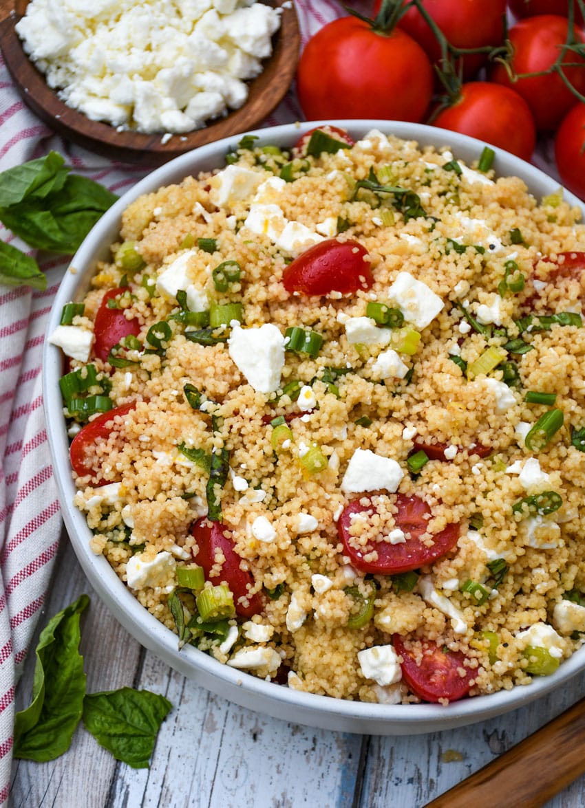 summer couscous salad in a gray serving bowl with fresh herbs on the side