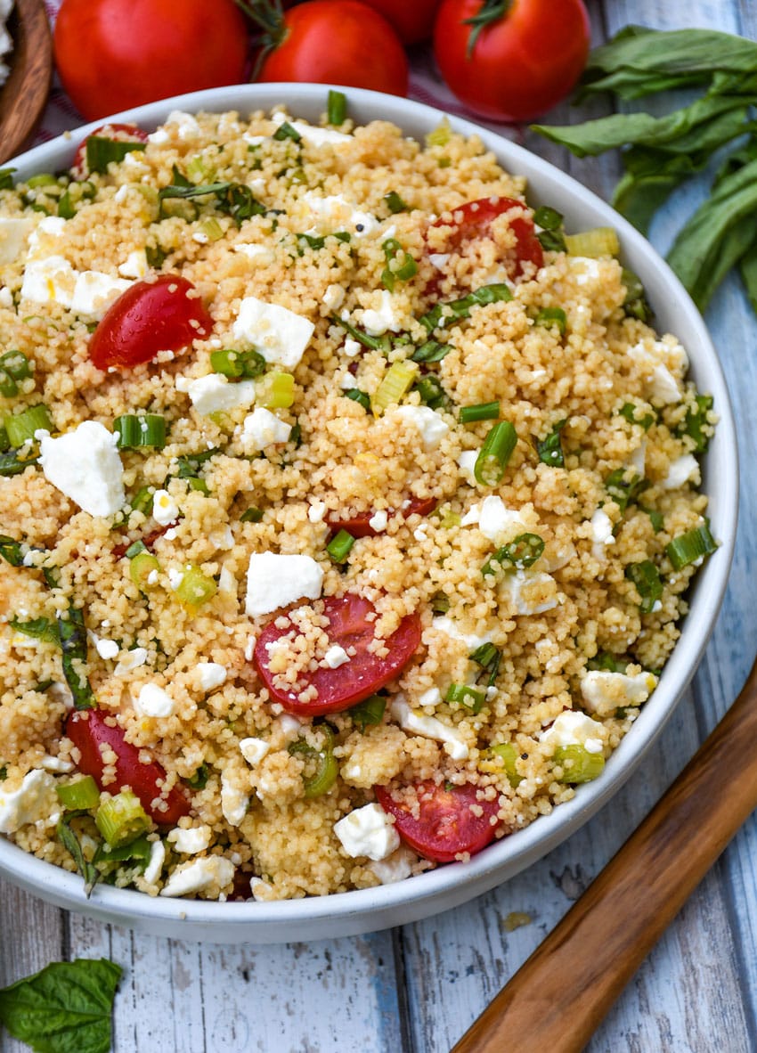 summer couscous salad in a gray serving bowl with fresh herbs on the side