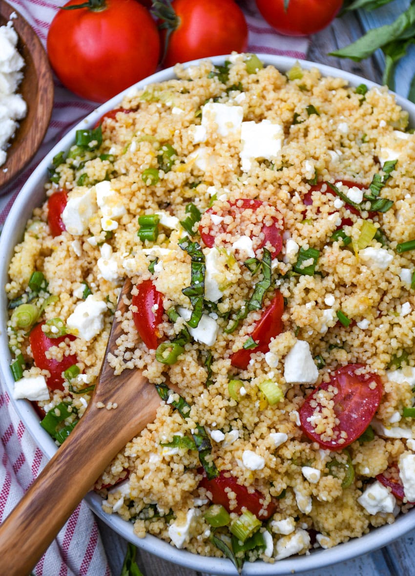 a wooden spoon scooping couscous salad out of a white serving bowl