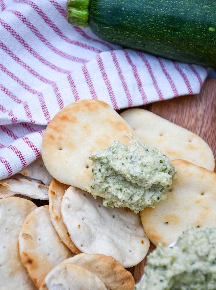 fresh zucchini hummus on a mini naan bread resting on a wooden cutting board