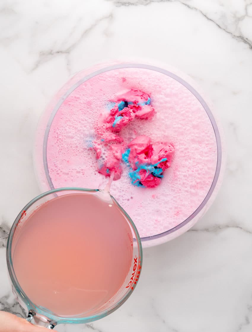 pink lemonade being poured over scoops of cotton candy ice cream in a glass punch bowl