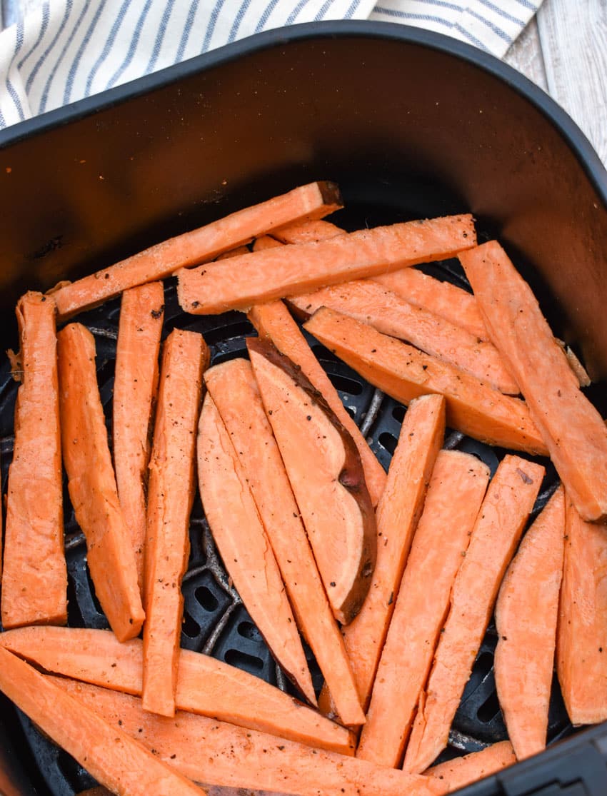 cut sweet potatoes coated in oil, salt, and pepper in the basket of an air fryer