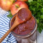 a small wooden spoon scooping homemade apple butter barbecue sauce out of a small glass jar