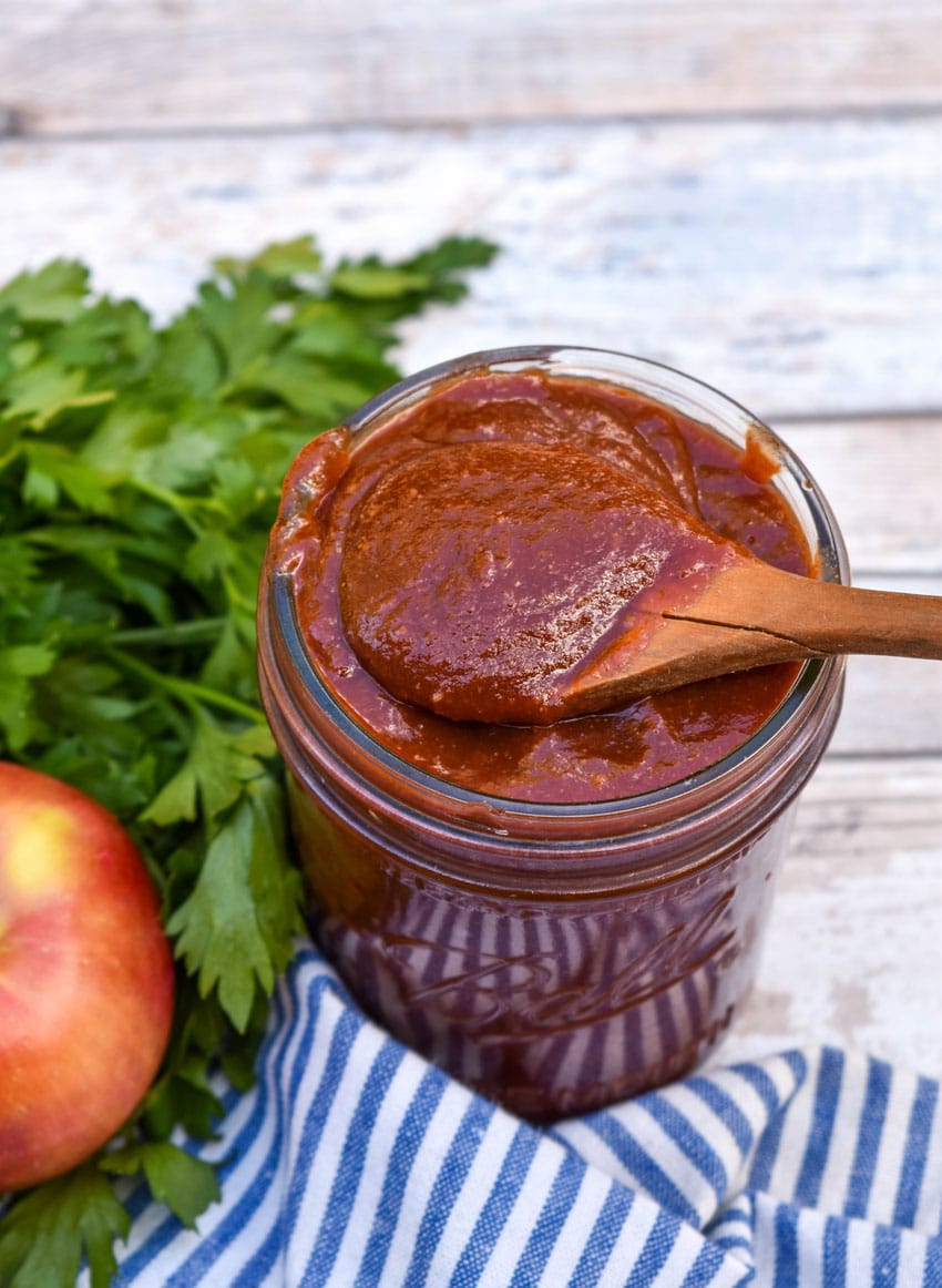 a small wooden spoon scooping homemade apple butter barbecue sauce out of a small glass jar