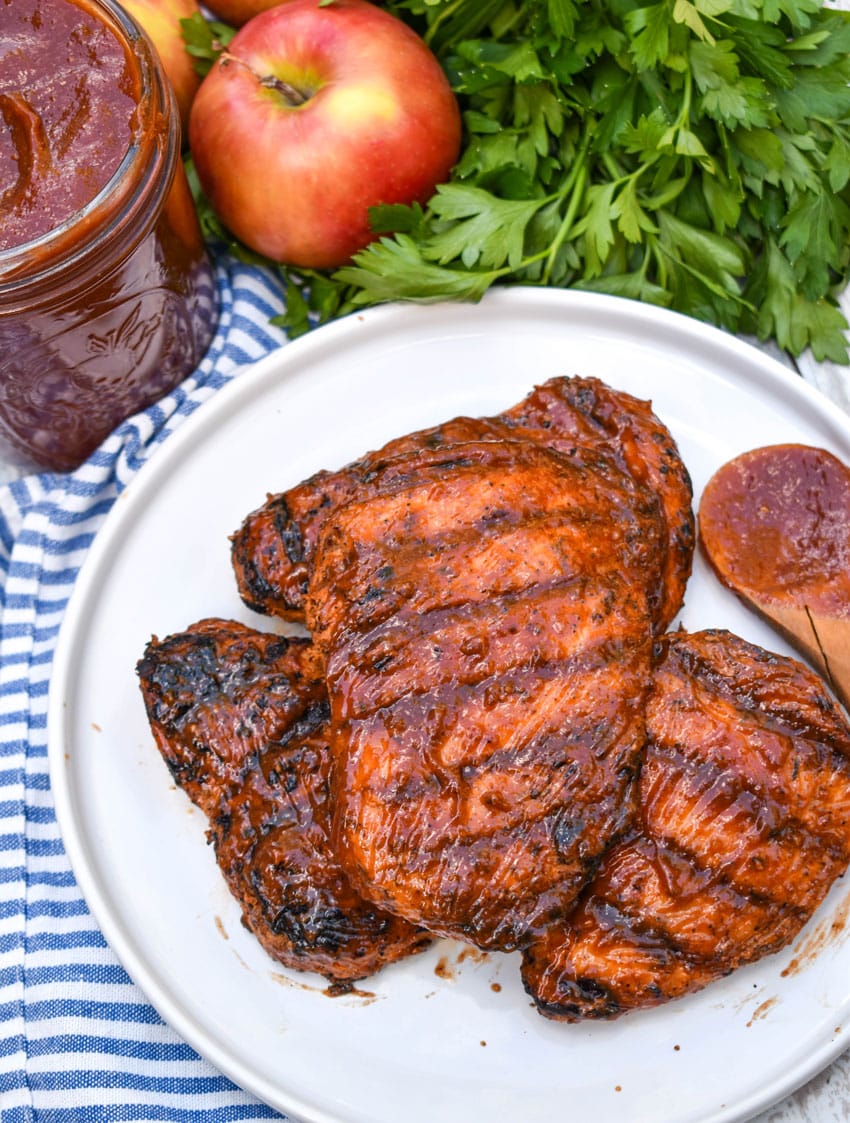 apple butter barbecue sauce coated grilled chicken breasts stacked on a white plate