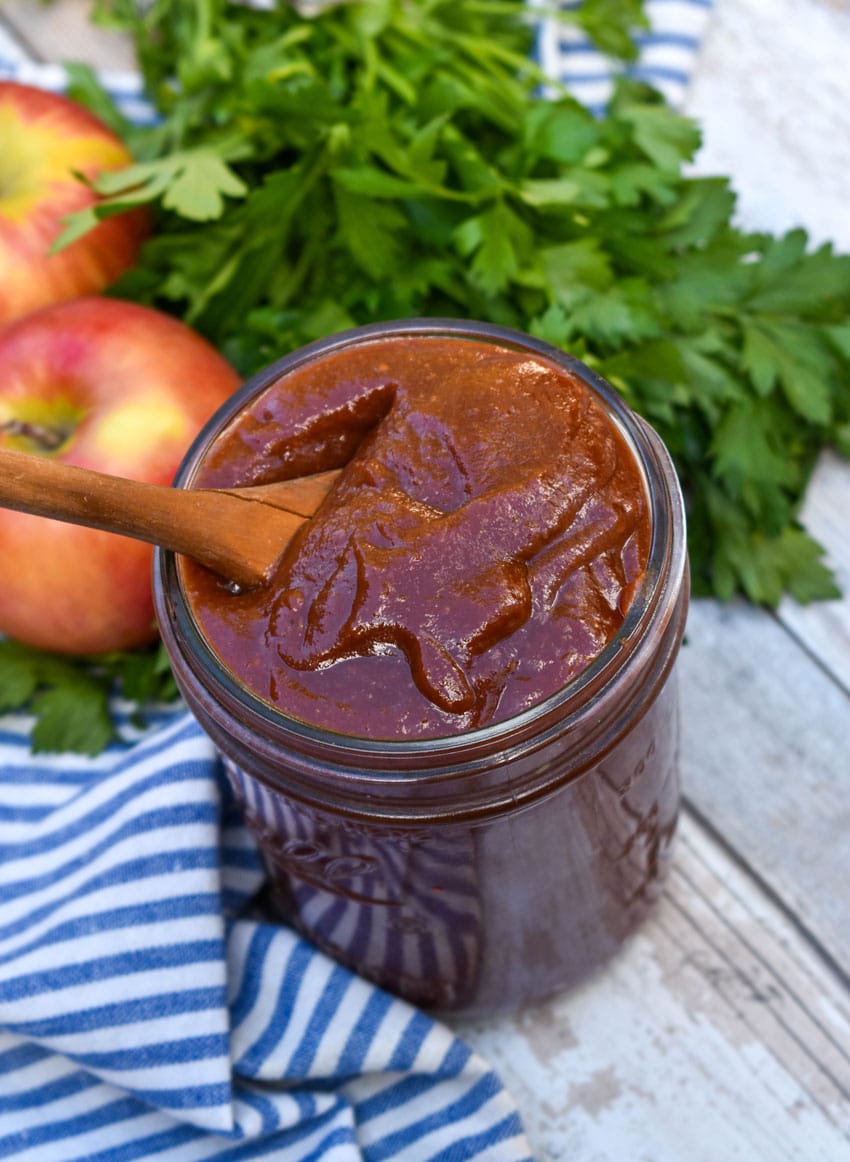 a small wooden spoon scooping homemade apple butter barbecue sauce out of a small glass jar