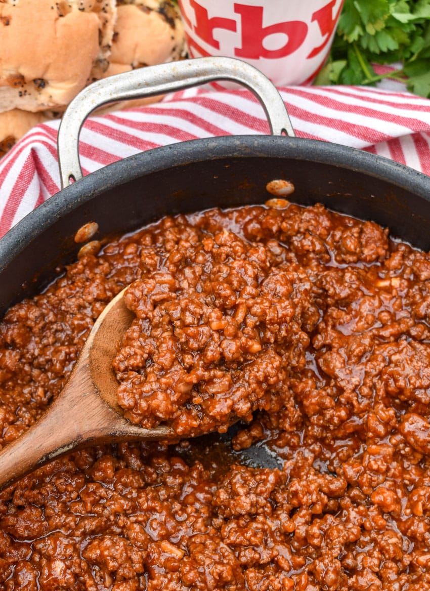 a wooden spoon scooping a homemade sloppy joe mixture out of a black skillet