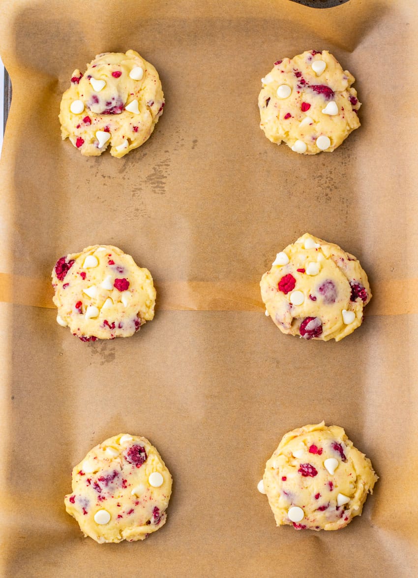 balls of raspberry cheesecake cookie dough arranged in two rows on a parchment paper lined baking sheet