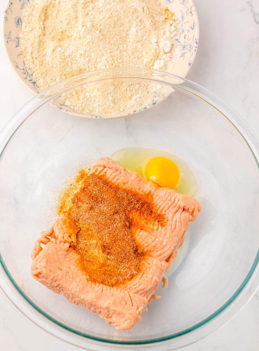 seasonings on top of ground chicken and egg in a glass mixing bowl