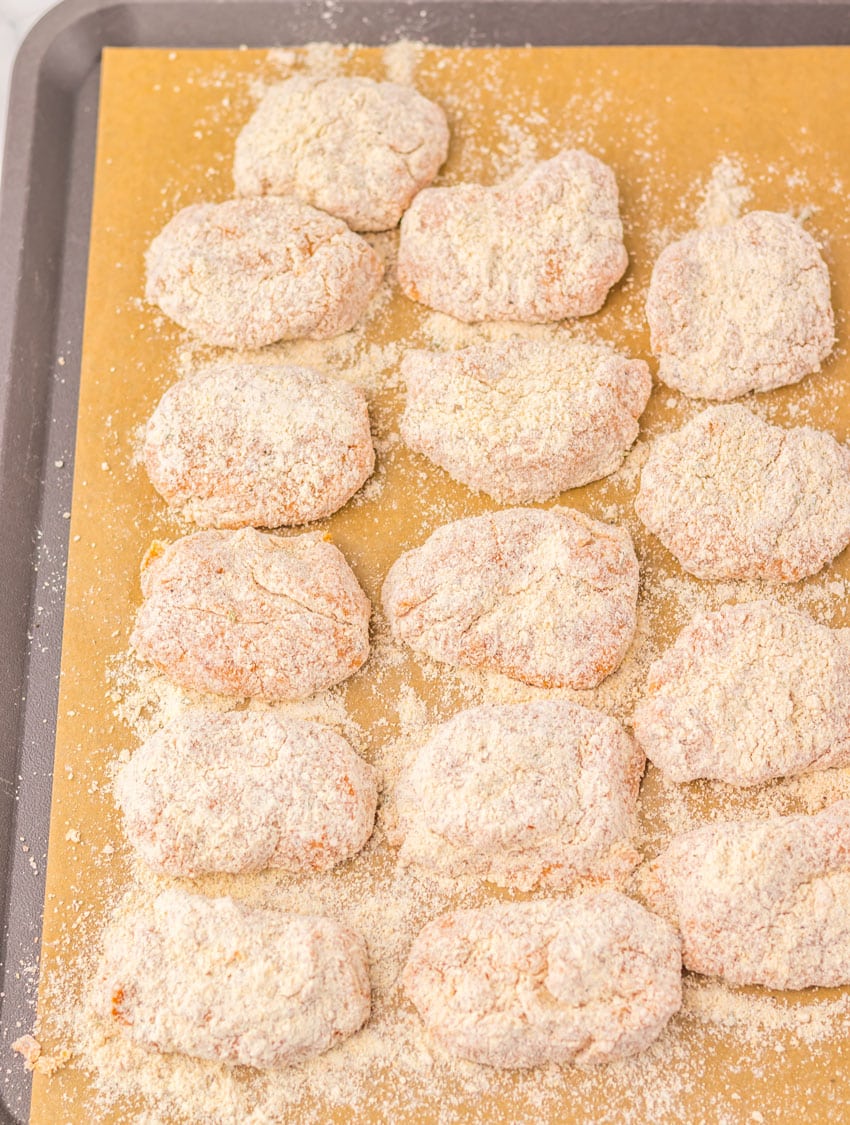 unbaked homemade breaded chicken nuggets arranged in rows on a parchment paper lined baking sheet