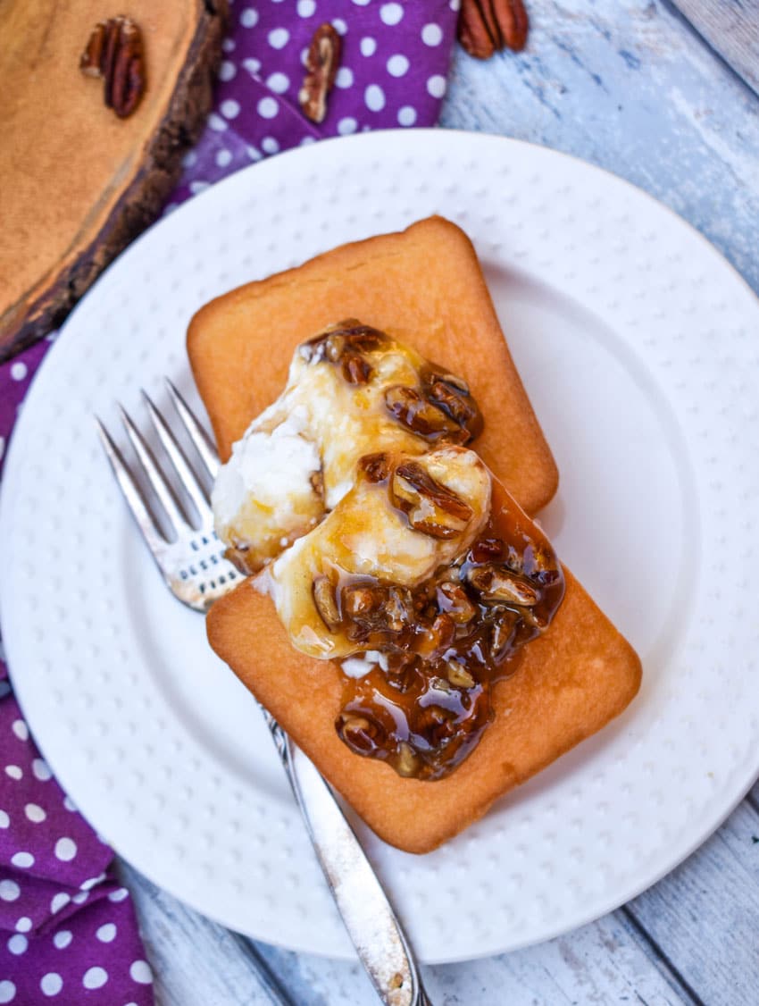 pecan pie dip spooned over two small pound cake squares on a small white dessert dip