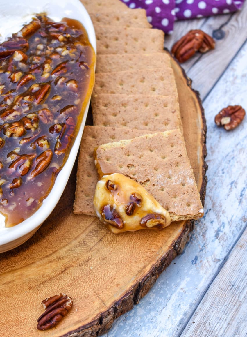 a graham cracker square topped with pecan pie dip resting on a wooden cutting board