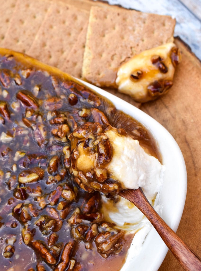 a wooden spoon scooping pecan pie dip out of a white serving dish
