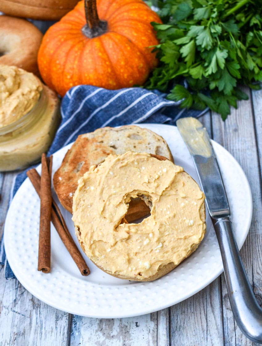 two halves of a toasted bagel spread with homemade pumpkin cream cheese spread on a small white plate
