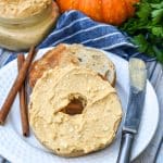 two halves of a toasted bagel spread with homemade pumpkin cream cheese spread on a small white plate