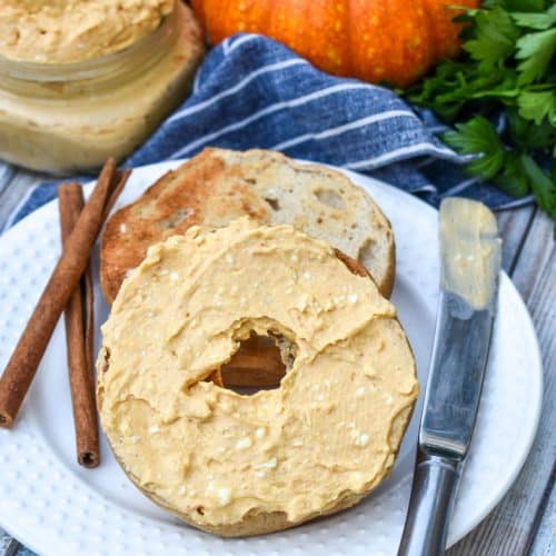 two halves of a toasted bagel spread with homemade pumpkin cream cheese spread on a small white plate