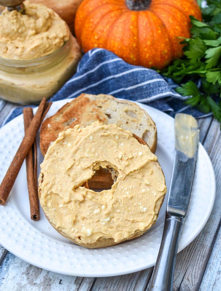 two halves of a toasted bagel spread with homemade pumpkin cream cheese spread on a small white plate