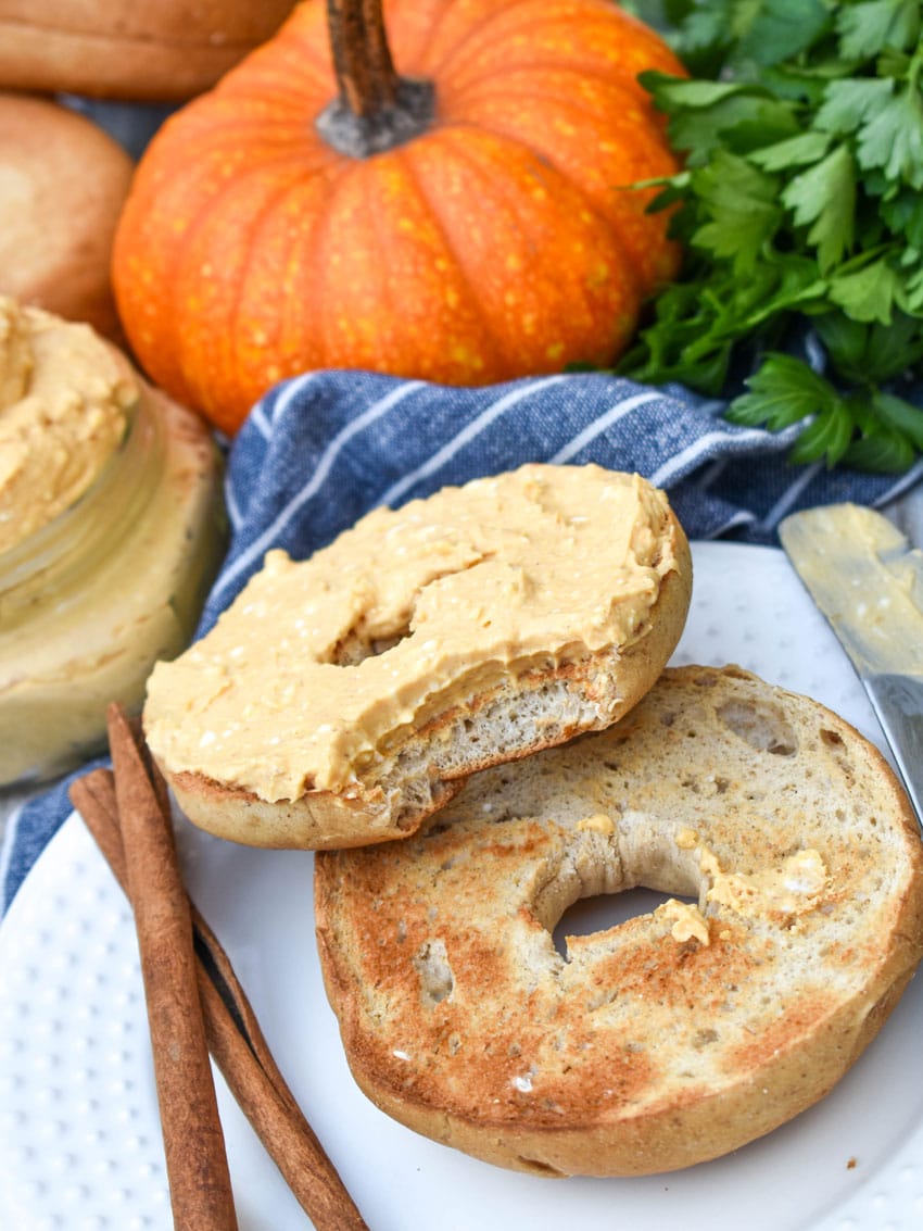 two halves of a toasted bagel spread with homemade pumpkin cream cheese spread on a small white plate