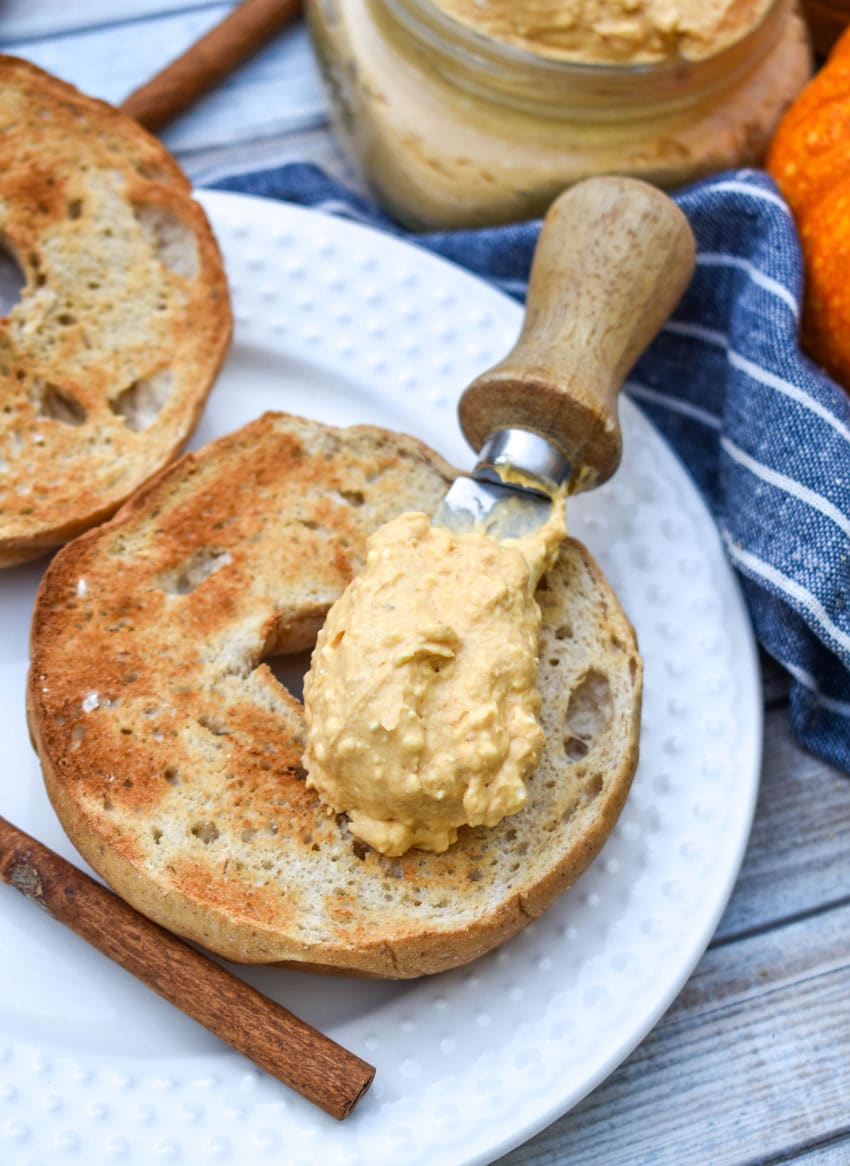 a small spreader holding a scoop of easy pumpkin cream cheese spread resting on top of a toasted bagel