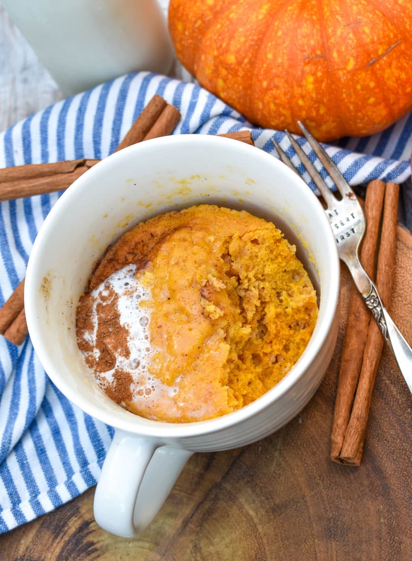 a microwave pumpkin mug cake on a wooden serving board with cinnamon sticks on the side