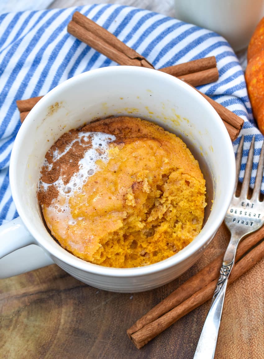a microwave pumpkin mug cake on a wooden serving board with cinnamon sticks on the side
