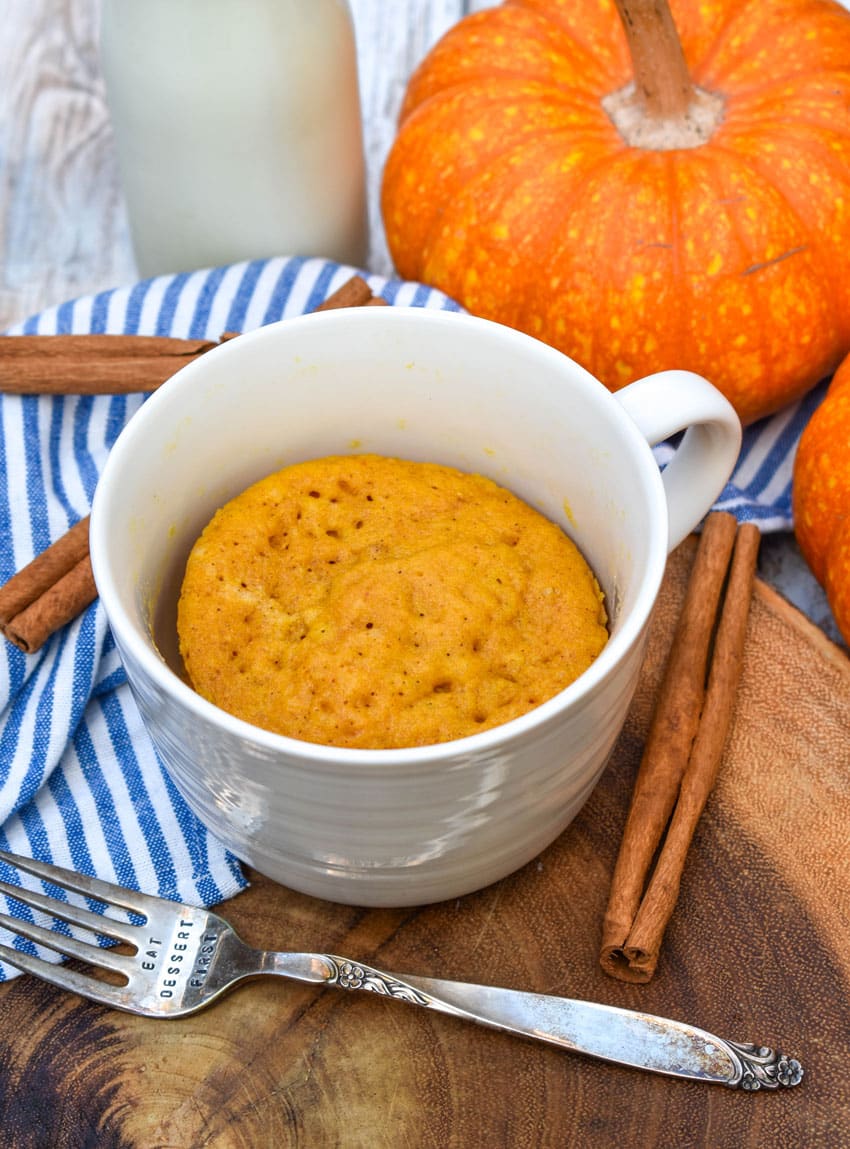 a microwave pumpkin mug cake on a wooden serving board with cinnamon sticks on the side