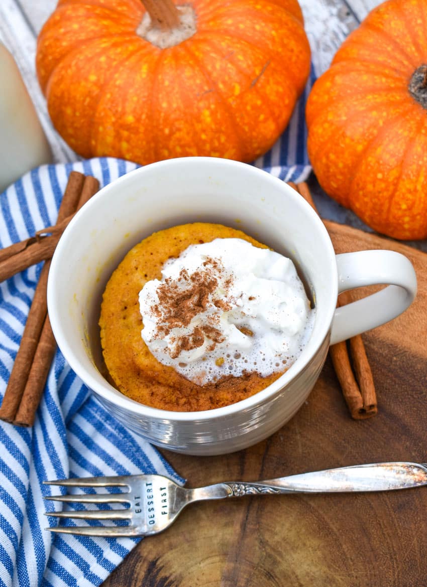 a microwave pumpkin mug cake on a wooden serving board with cinnamon sticks on the side