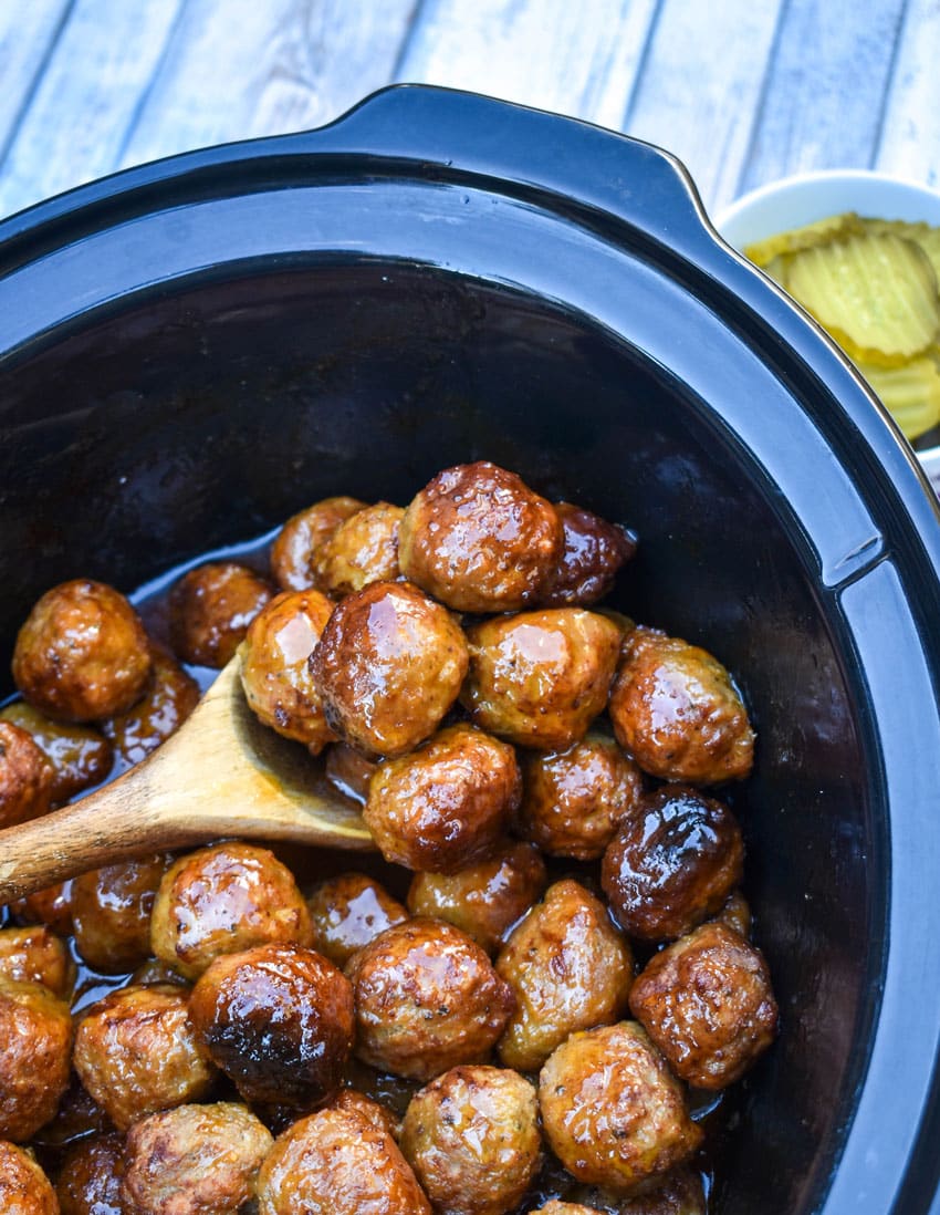 a wooden spoon scooping hot honey meatballs out of a black crock pot