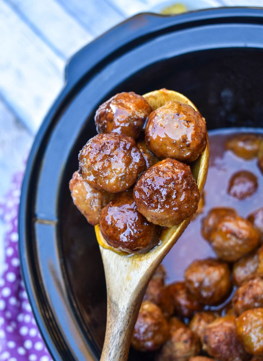 a wooden spoon holding up a scoop of slow cooker hot honey meatballs