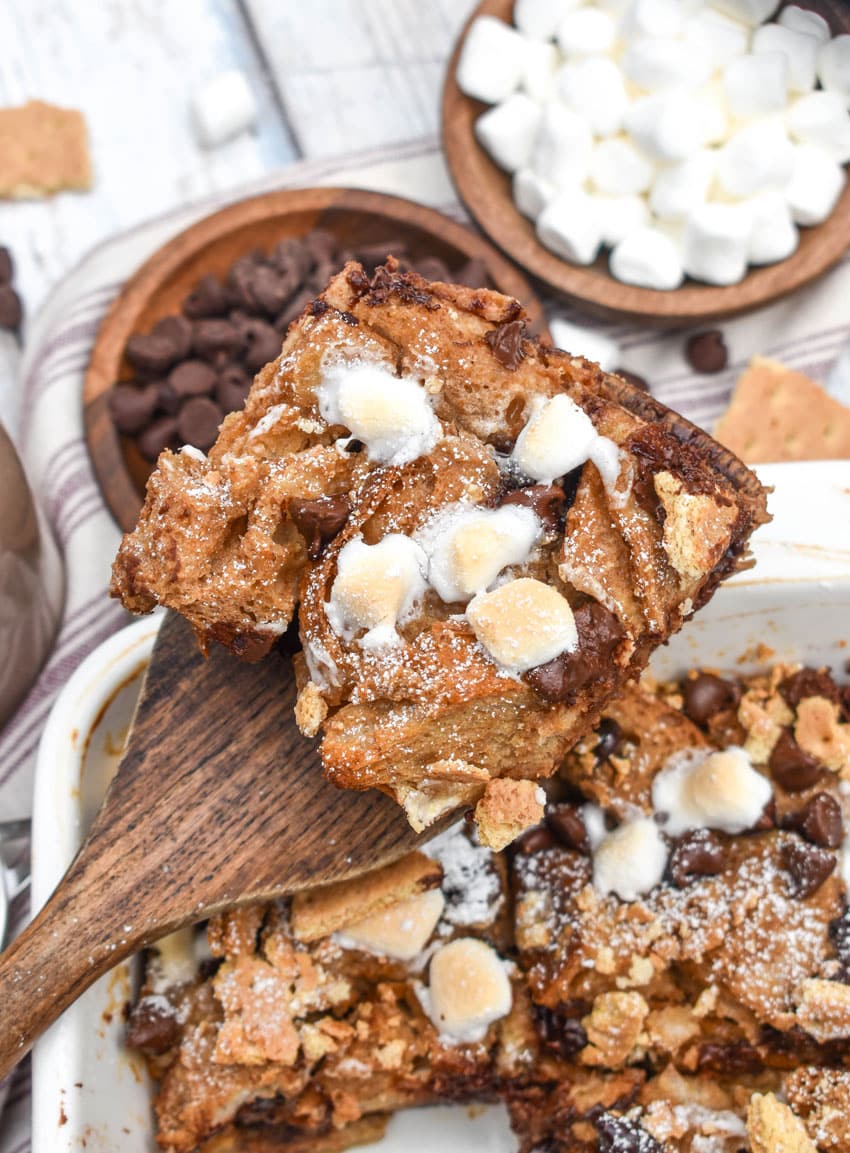 a wooden spatula holding up a slice of a s'mores french toast bake