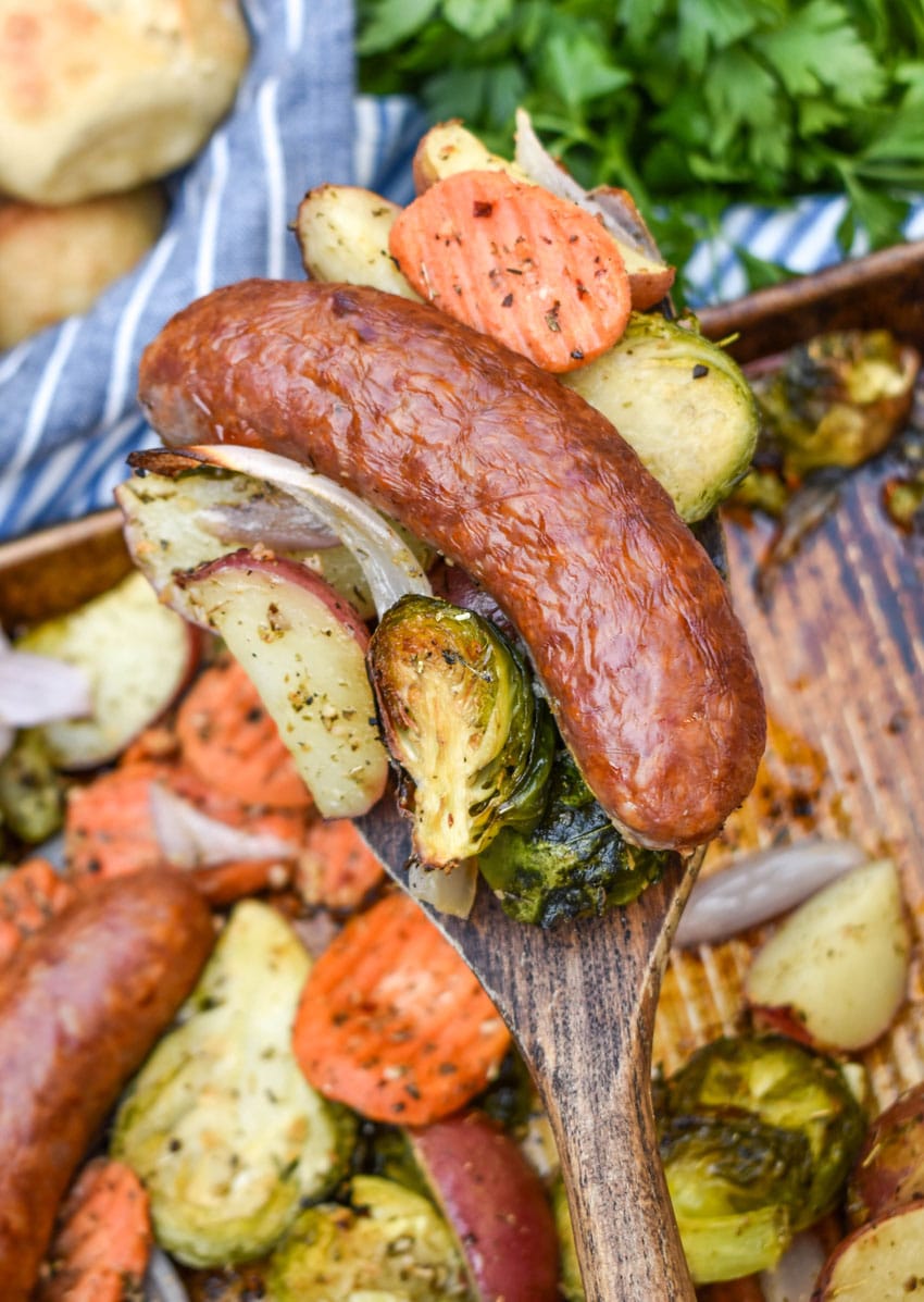 a wooden spatula holding up a scoop of sheet pan sausage and vegetables