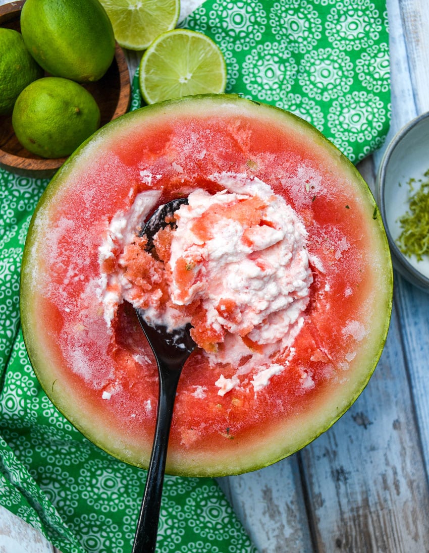 a black metal spoon scraping the inside of a watermelon and cold cream together