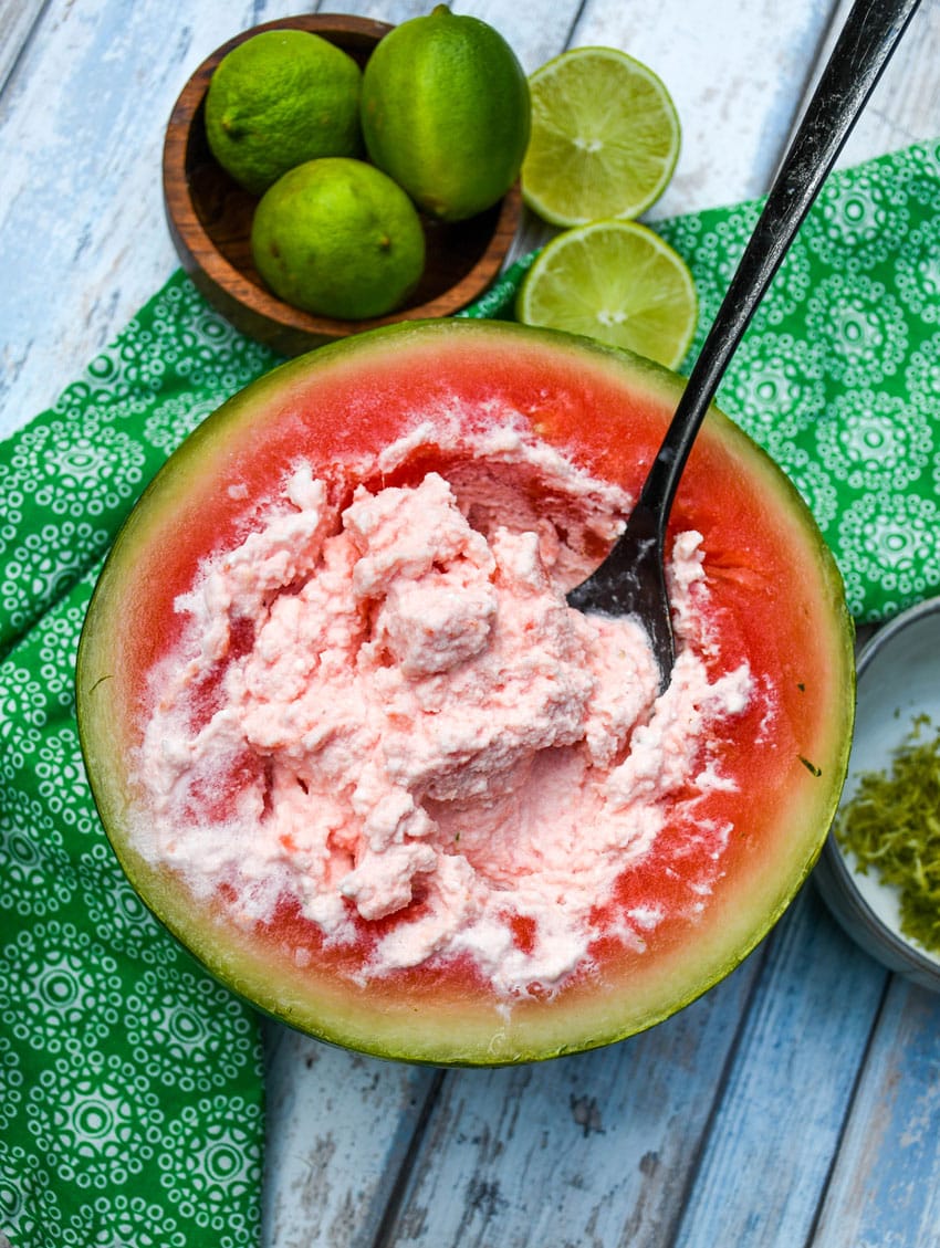 a black metal spoon scraping the inside of a watermelon and cold cream together
