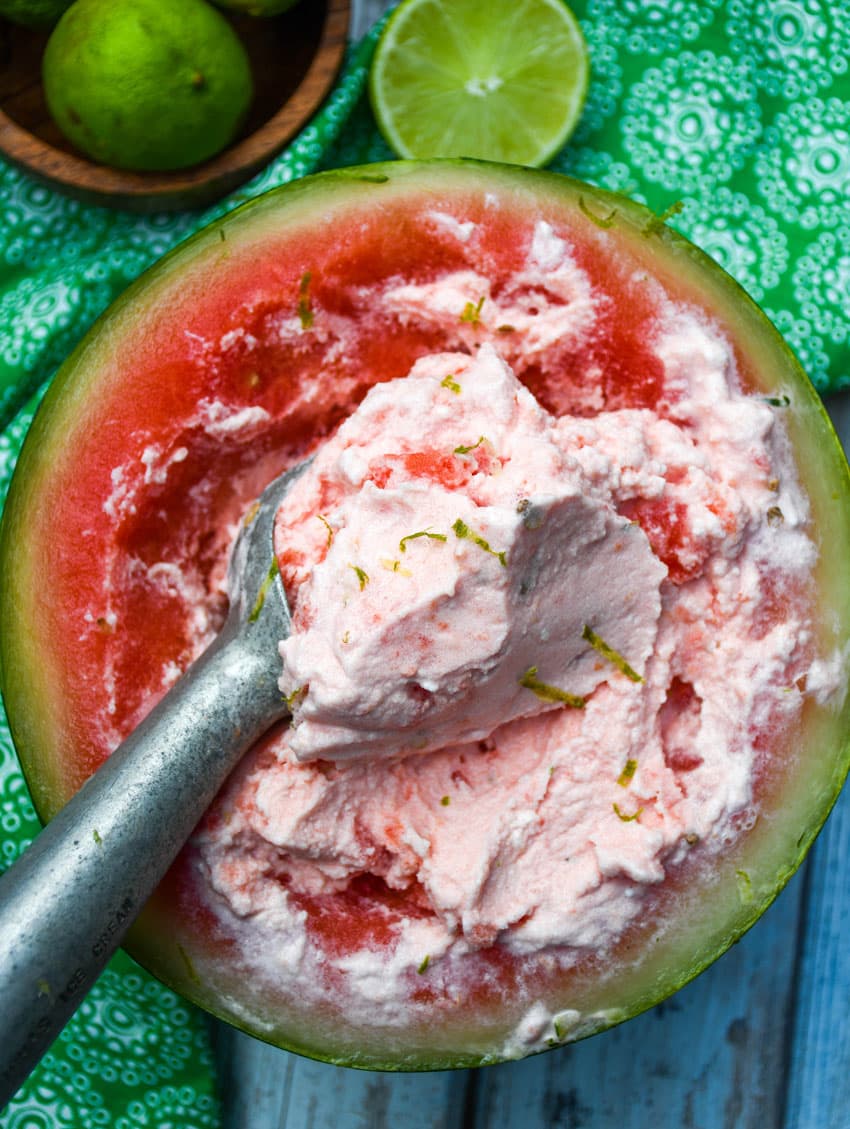 a metal ice cream scoop scooping homemade watermelon ice cream out of a watermelon bowl