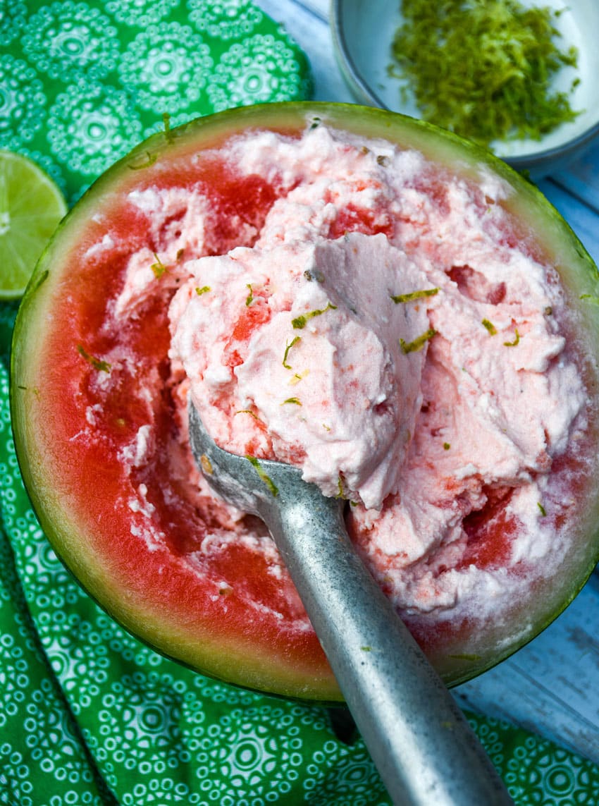 a metal ice cream scoop scooping homemade watermelon ice cream out of a watermelon bowl