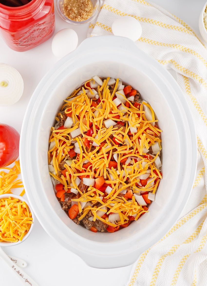 breakfast casserole ingredients spread in the bottom of a white slow cooker