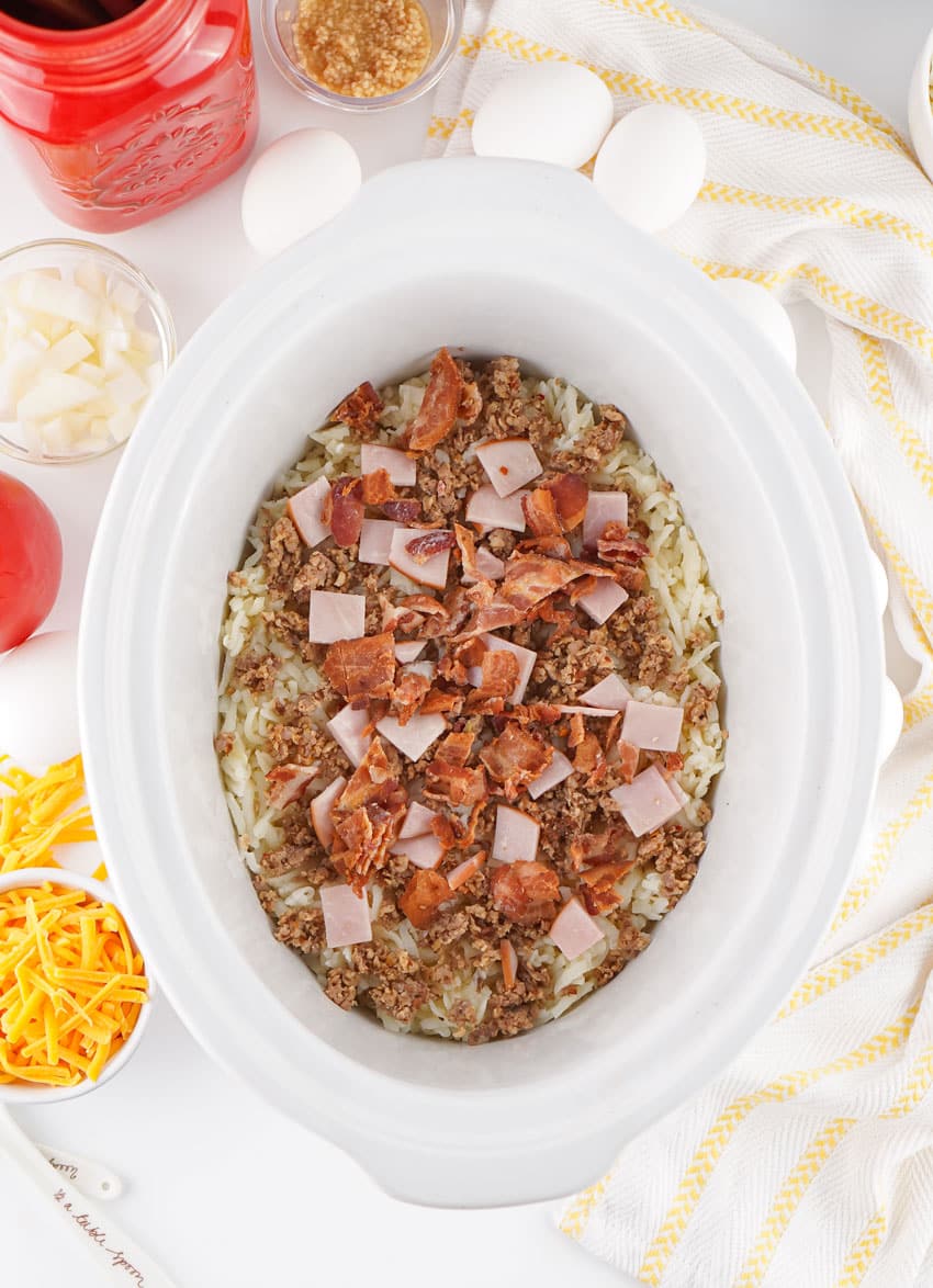 breakfast casserole ingredients spread in the bottom of a white slow cooker