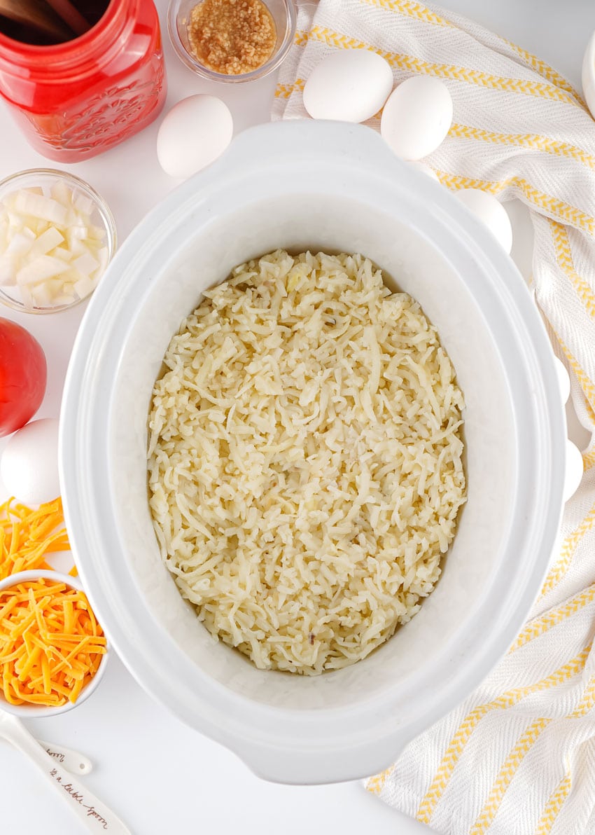 shredded hash browns spread in an even layer in the bottom of a white crockpot