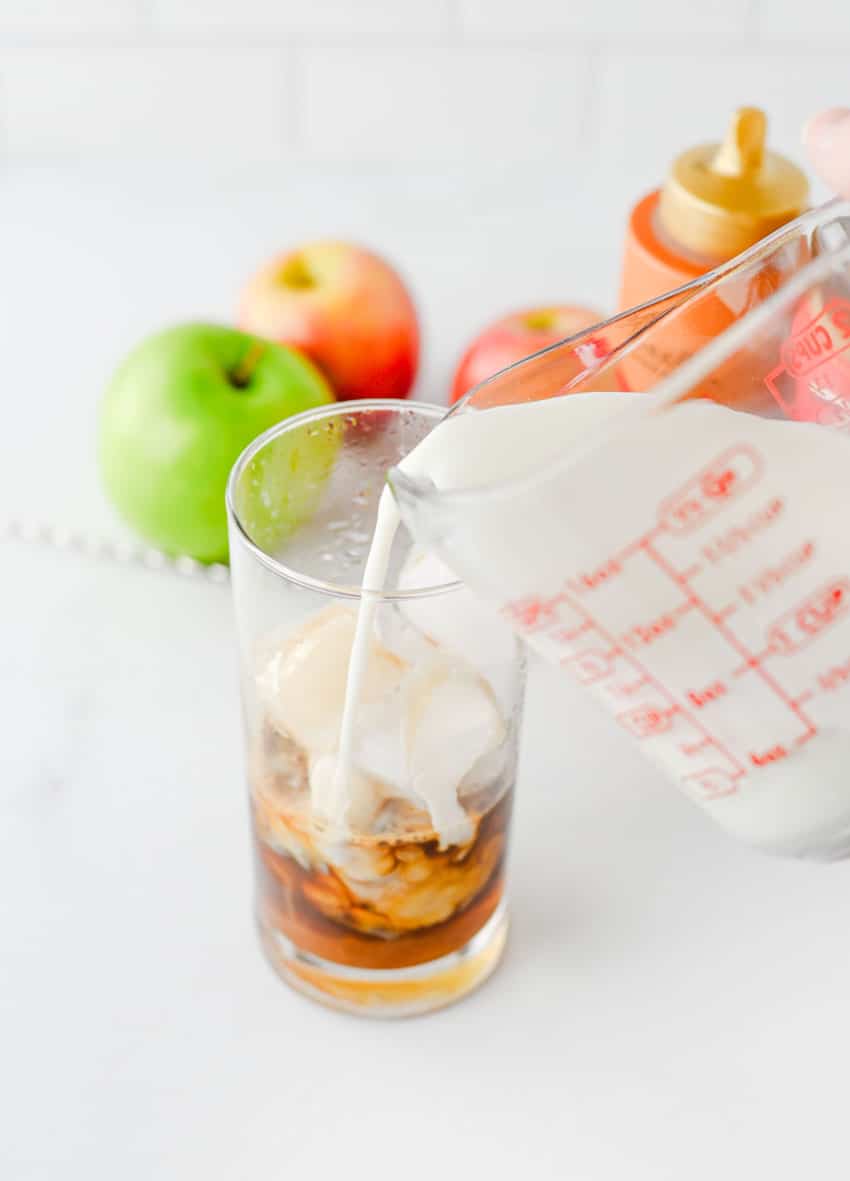 milk being poured into espresso over ice cubes in a small glass jar