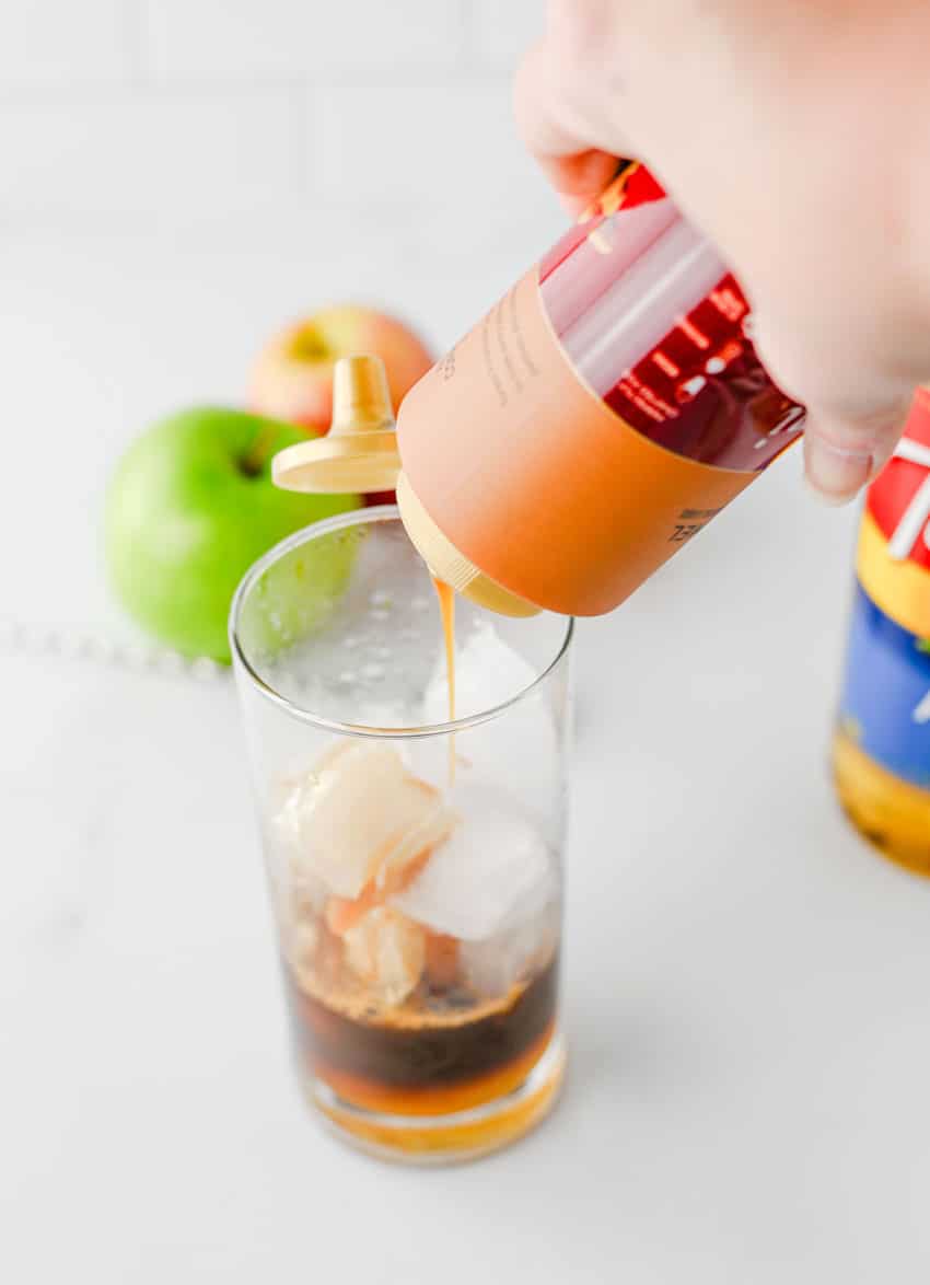 caramel sauce being poured into espresso over ice in a small glass jar