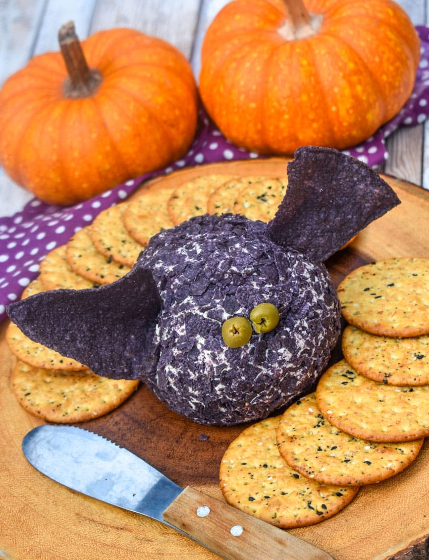 a halloween themed bat cheese ball surrounded by crackers on a wooden serving board