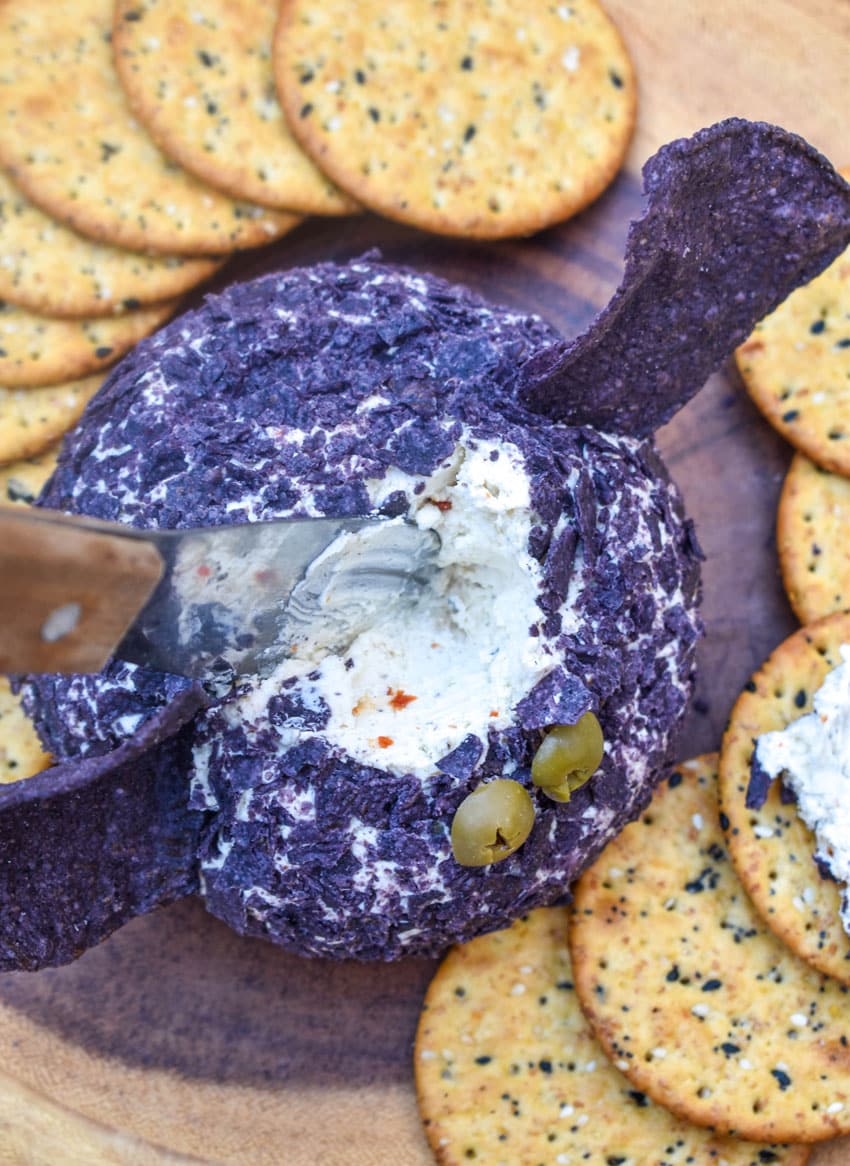 a wooden handled cheese knife inserted into an italian cheese ball coated with blue corn tortilla chip crumbs