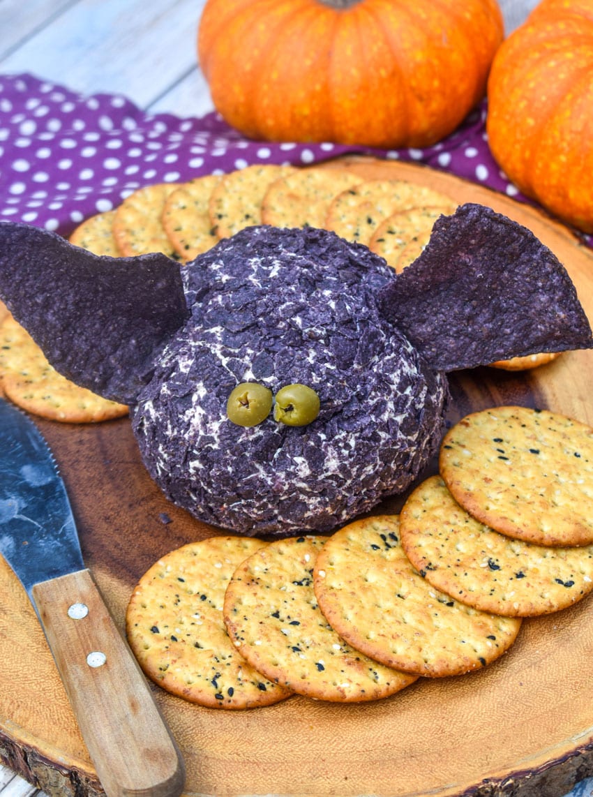 a halloween themed bat cheese ball surrounded by crackers on a wooden serving board
