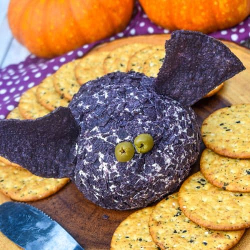 a halloween themed bat cheese ball surrounded by crackers on a wooden serving board