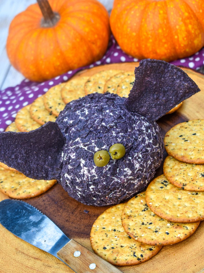 a halloween themed bat cheese ball surrounded by crackers on a wooden serving board